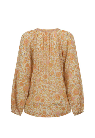 A long-sleeve blouse with a gathered, pleated back neckline, featuring an all-over floral pattern in shades of orange, yellow, and beige on a white background.