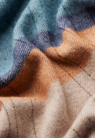 A close-up of a soft woven textile with a plaid pattern in muted blue, peach, and warm beige tones.